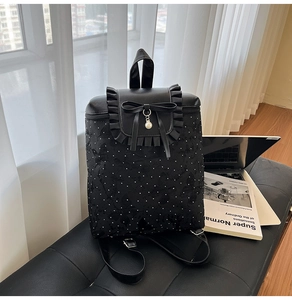 Detail of black polka dot backpack with ruffled leather flap, bow, and pearl charm