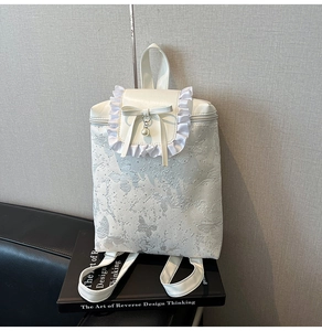 Detailed view of white backpack with butterfly relief, lace edges, and pearl charm