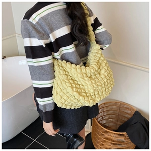 Detail view of a pale yellow pleated puffer shoulder bag worn over a casual outfit