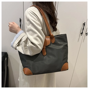 Detail of dark green nylon tote with brown leather handles worn by a model in casual style