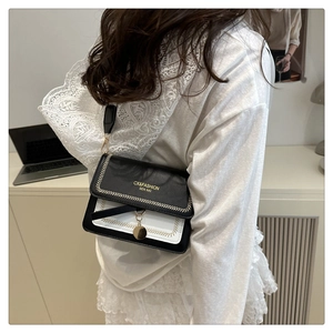 Detail of contrast color crossbody bag featuring gold embroidery and metal pendant charm