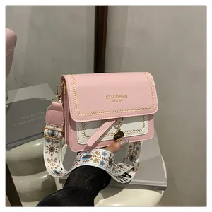 Detail of pink and white crossbody bag with stylish embroidery wide strap and gold charm