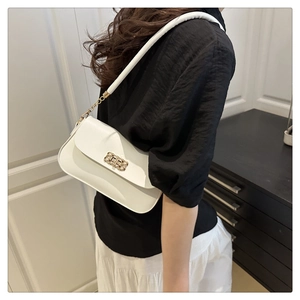 Detail of white leather crossbody bag with golden textured lock on model's shoulder