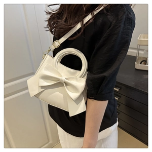 Close-up of white PU leather handbag featuring a large bow and gold metal hardware