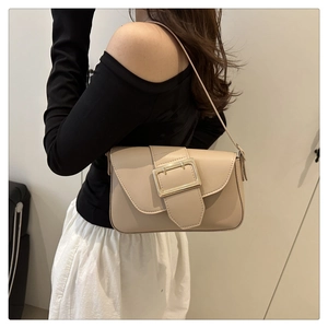 Detail of minimalist beige faux leather baguette bag with a gold buckle worn by model