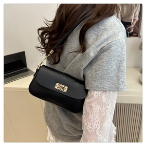 Detail of black rectangular crossbody bag featuring a golden decorative clasp and chain strap