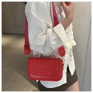 Detail of red crossbody bag with wide strap and gold hardware on white shirt model