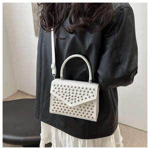 Detail shot of white crossbody bag with silver studs on a model in a black leather jacket
