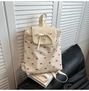 Detailed shot of beige leather backpack flap with decorative bow and pearl pendant