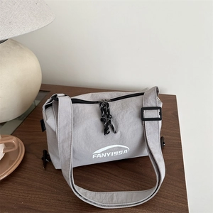 Light gray nylon crossbody bag with letter print on a wooden desk in a cozy room
