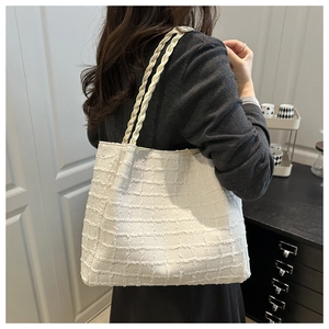 Detail of a beige woven tote bag with artistic braided straps shown on a female model