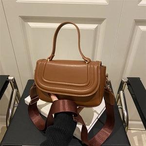 Brown leather crossbody bag with quilted flap and wide nylon strap on chair