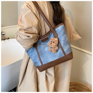 Dettaglio della borsa tote in denim blu con finiture in pelle marrone e ciondolo orsetto
