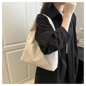 Close-up of beige lychee grain leather tote bag worn by model in black shirt