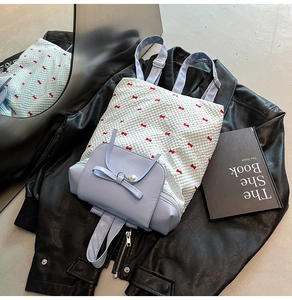 Detail of lavender backpack featuring bow prints and a pearl pendant on a black leather jacket