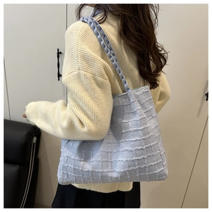 Detail of light blue textured tweed tote bag with woven shoulder strap on a model