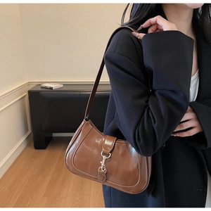 Détail de la texture en cuir verni marron et du fermoir piston en métal sur le sac à épaule