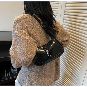 Détail d'un sac demi-lune en cuir verni noir avec boucle argentée porté par un modèle