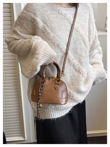 Detail of a brown shell-shaped leather crossbody bag with a decorative woven pendant