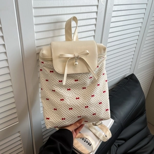 Off-white bubble textured backpack with red bows and pearl charm in a casual hand-held view