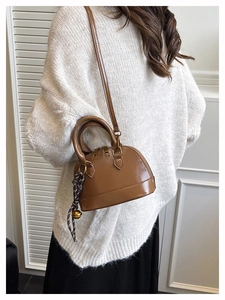 Brown shell-shaped crossbody bag shown on a model with a white sweater and skirt