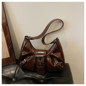 Detail of a brown glossy leather shoulder bag with a large silver buckle and vintage style