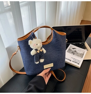 Details der blauen Denim-Tote-Bag mit braunem Lederbesatz und süßem Bärenanhänger