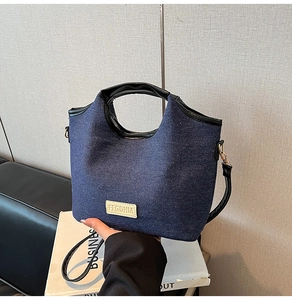 Detail der blauen Denim-Tasche mit schwarzen Ledergriffen und goldenen Metallschnallen