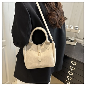 Elegante borsa a secchiello crema con chiusura dorata indossata da modella con blazer nero