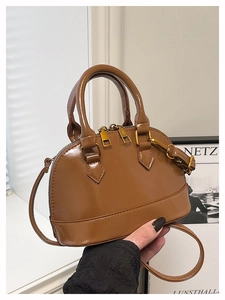 Detail of a brown glossy shell bag with golden zippers and adjustable shoulder strap
