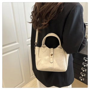 Borsa a secchiello in pelle beige con chiusura dorata su outfit con blazer nero