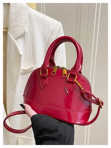 Detail of glossy red shell bag with gold hardware and dual zippers in model's hand