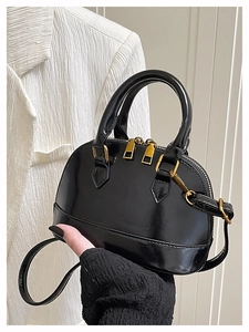Close-up of black shell handbag with glossy finish and golden metal zipper details