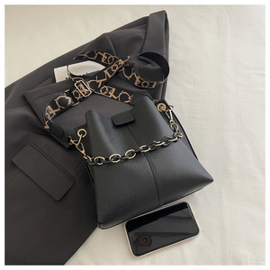 Detail of black textured bucket bag with chain decoration and patterned wide strap