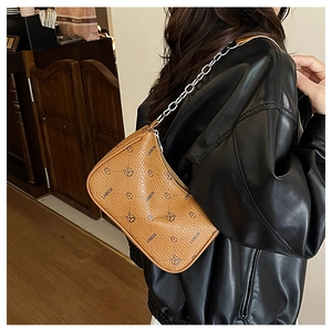 Detail der braunen Schultertasche aus genarbtem Leder mit Kette und Muster am Modell