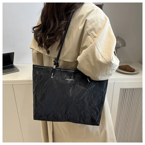 Detail of black textured tote bag featuring a silver metal logo and long shoulder straps
