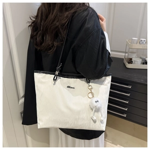 Detail of cream tote bag with black straps, metal logo, and plush monster charm pendant