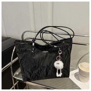 Dettaglio borsa tote nera plissettata con logo argento e ciondolo peluche bianco