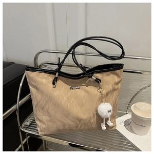 Dettaglio borsa tote beige a pieghe con tracolle nere e ciondolo peluche su supporto