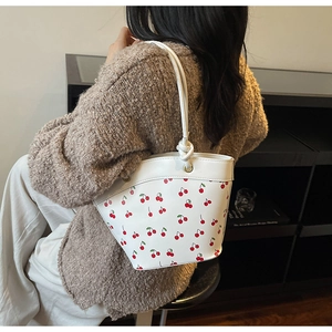 Close-up of white bucket bag featuring red cherry print and tied leather shoulder strap