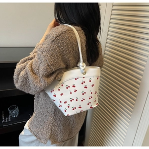 Detailed view of white bucket bag featuring red cherry prints and slim shoulder strap