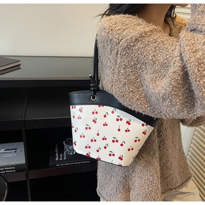 Detailed view of white cherry print tote bag with black leather strap on a model