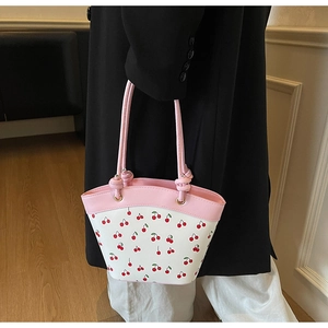 Detail of pink and white crossbody bag with cherry print on a model in a black coat