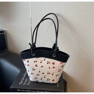 Close-up of cherry print tote bag with black leather handles on a minimal background