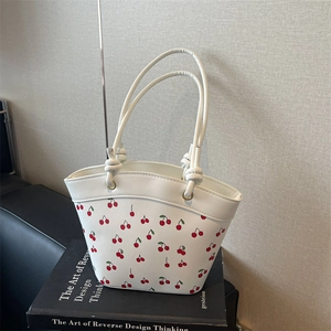 Minimalist white bucket bag with red cherry print and knotted handles on art book