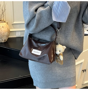 Brown patent leather handbag with white Logo tag and a cute plush bear charm detail