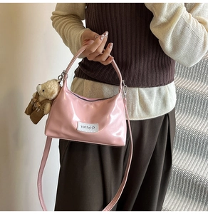 Detail view of pink patent leather handbag featuring a cute plush bear charm and brand label