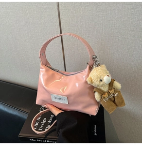 Detail of pink patent leather handbag with bear charm on a design book background