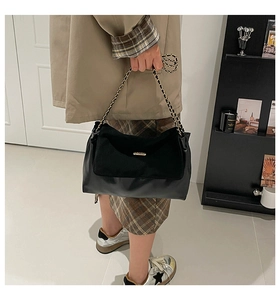 Detail of black suede patchwork tote bag featuring golden chain strap and smooth leather
