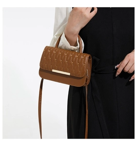 Brown crossbody bag with wave quilting and gold metal bar detail on a model
